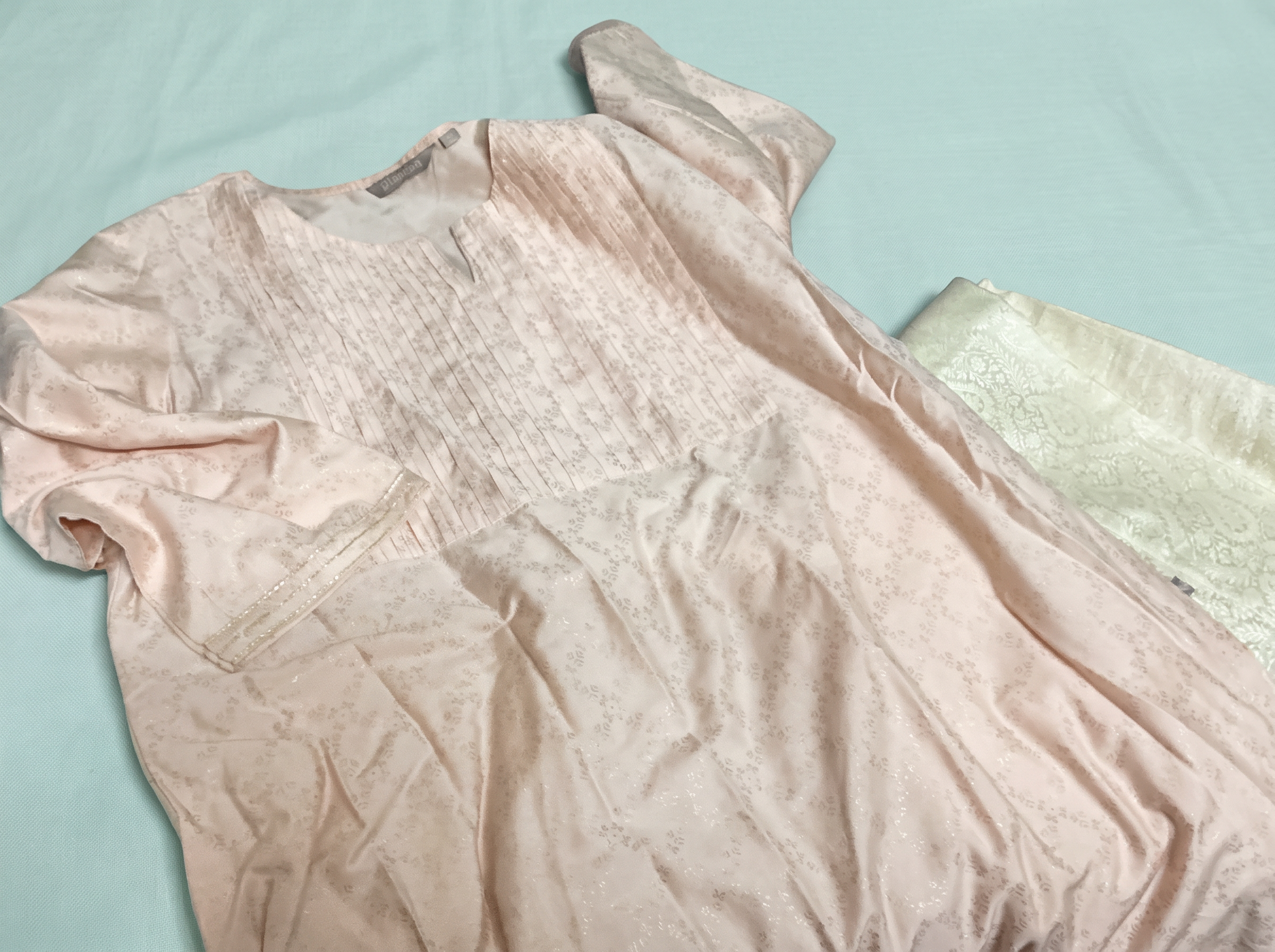 A blush pink kurta and sheer dupatta laid out on a soft teal cloth